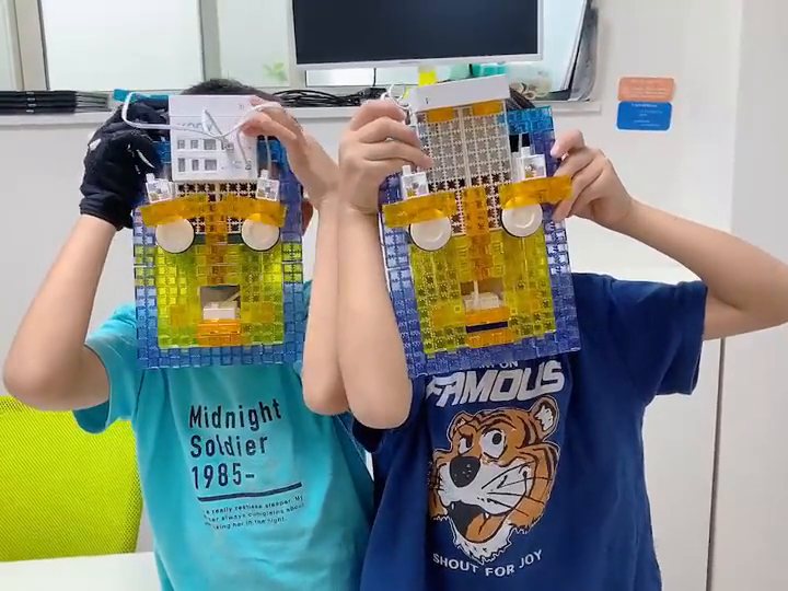 ブロックで顔の形をつくった作品「変な顔」を、2人の子どもが顔の前に持って見せている様子
