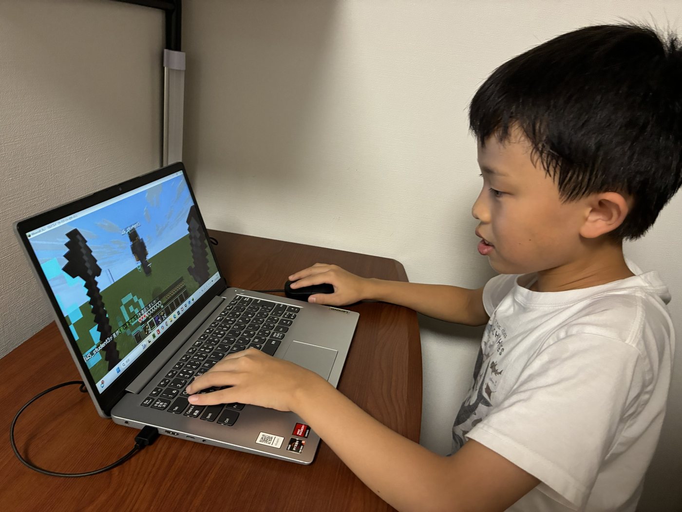 ノートパソコンでマインクラフトの画面を見ながら、キーボードとマウスを操作する子ども