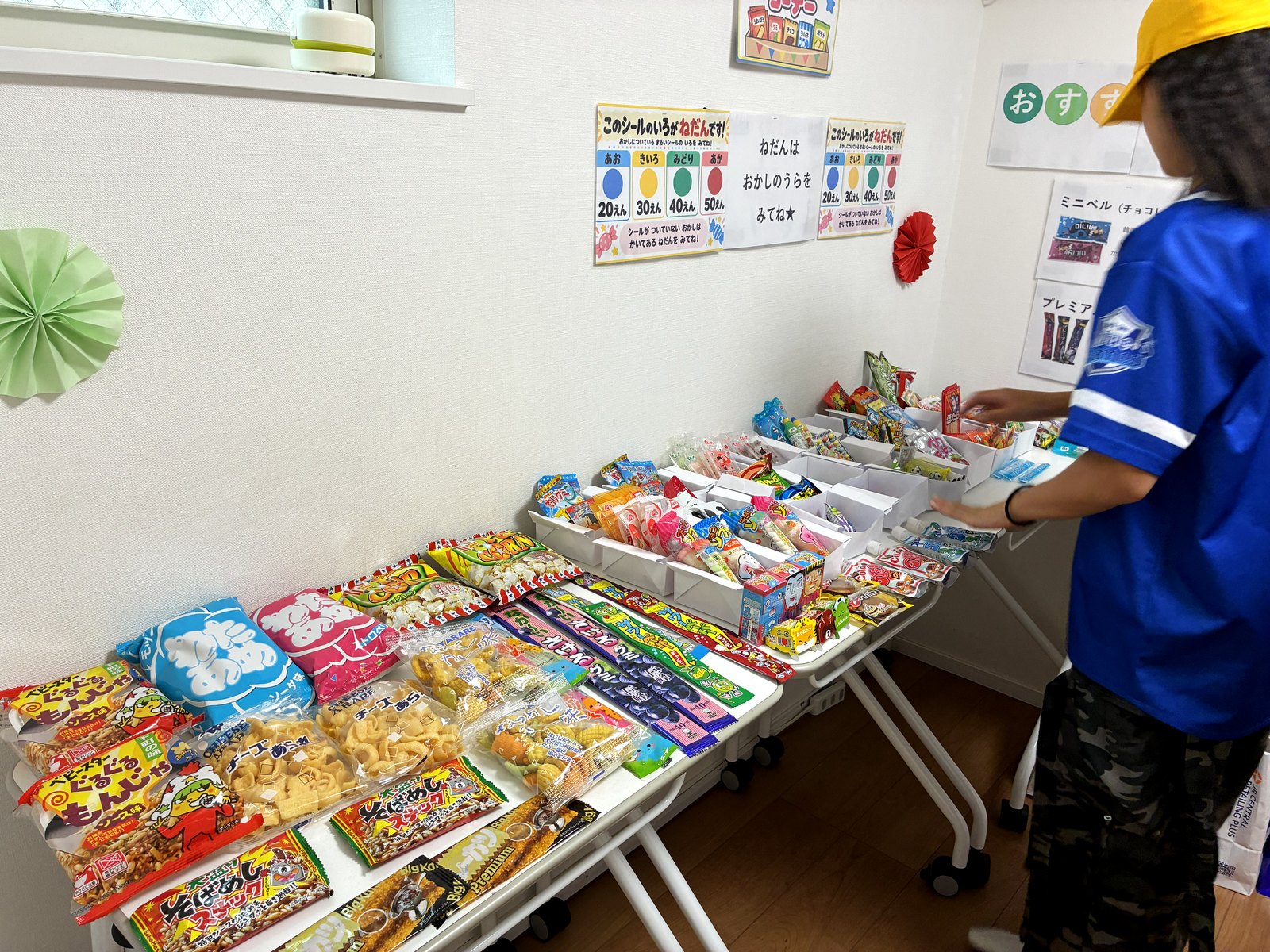 たくさんの駄菓子が並ぶ秋祭りの駄菓子屋。台の奥にはお店の側に立つ子ども
