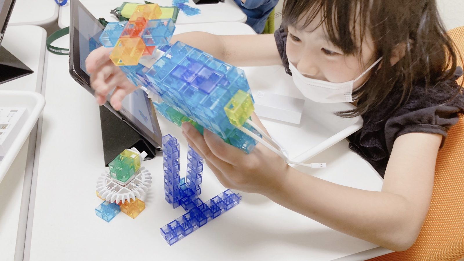 大きな青いKOOVのロボット作品に手を添えて組み立てる子ども