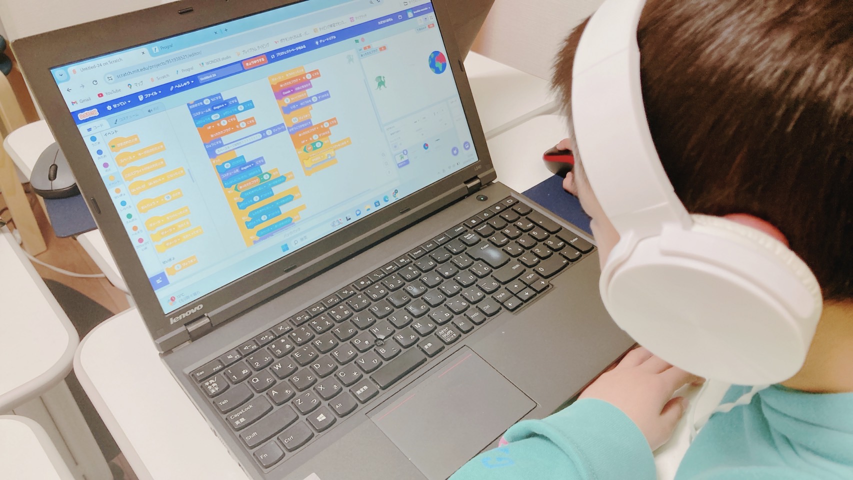 ヘッドホンをつけて、パソコンでScratchのプログラムを組む子ども