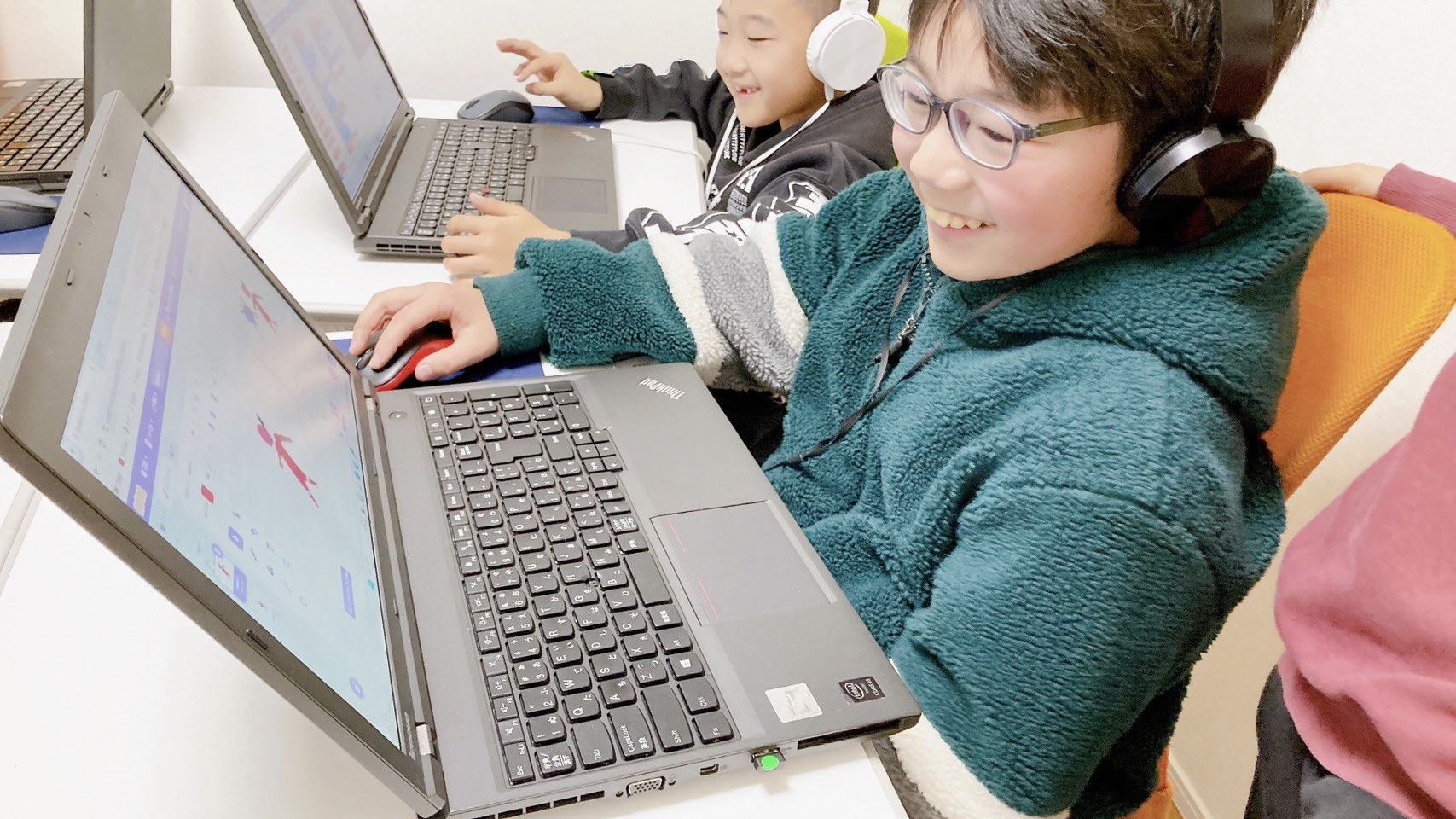 ヘッドホンをつけ、笑顔でパソコンのプログラミングに取り組む子どもたち